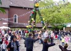 Ein Pfingstenkranz in Oelde, der mit bunten Bändern und Luftballons geschmückt ist. Die Menschen feiern, singen und tanzen.