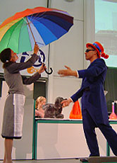 Mister Technicolor überreicht Dorothy den Regenbogenschirm und stellt sie vor ein Rätsel.